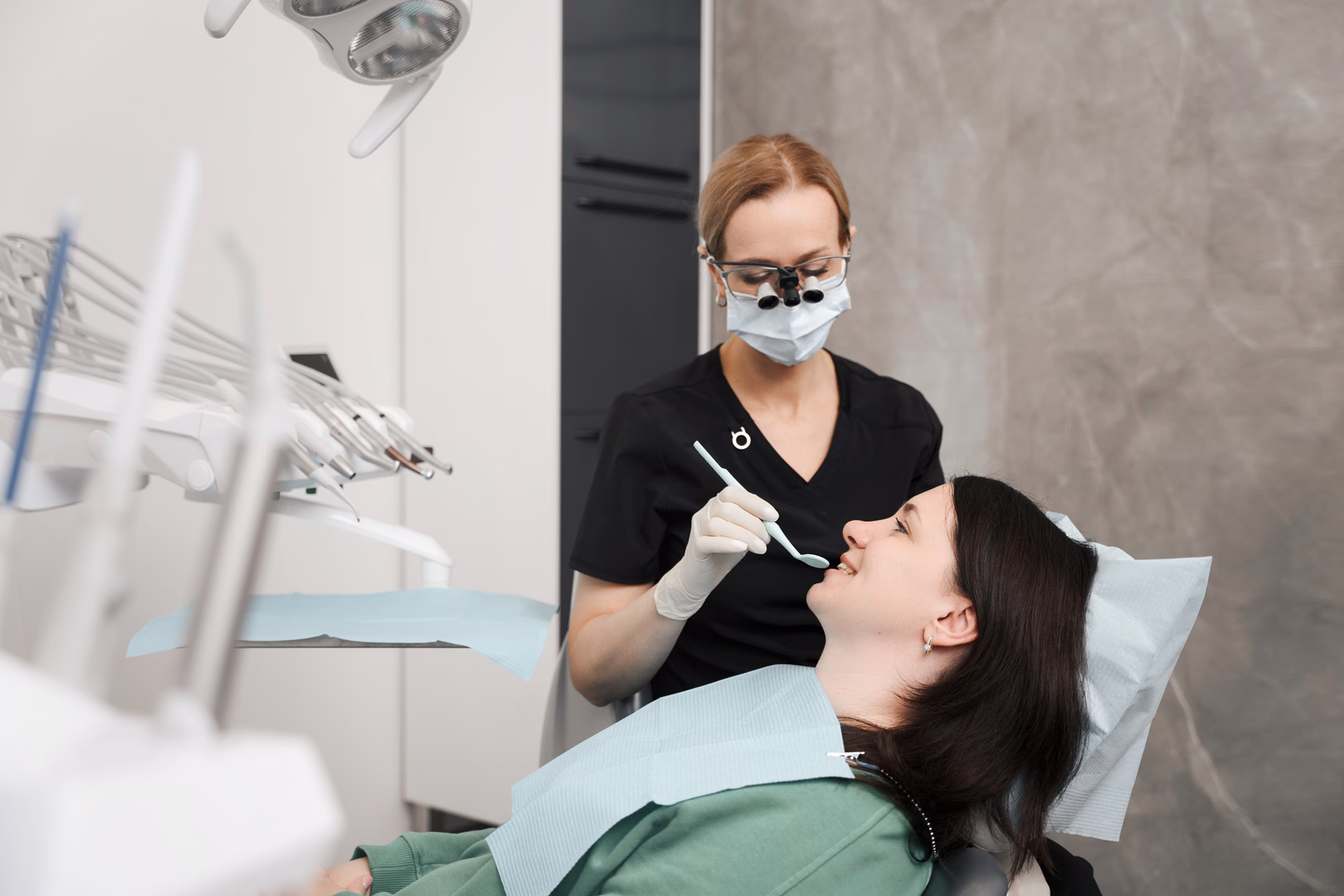 Сотрудница Dental Smile в маске и увеличительных очках осматривает пациентку в кресле