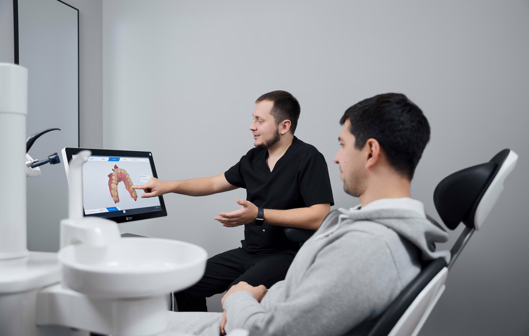 Стоматолог Weeksmile показывает цифровую модель зубов пациенту в кресле, вид сбоку