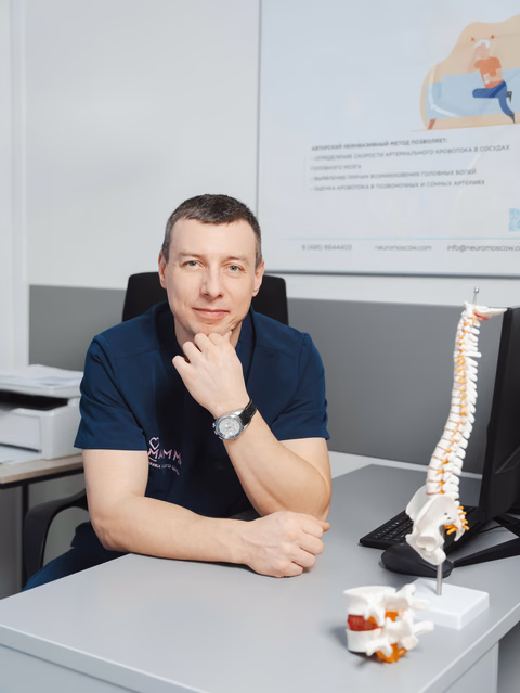 Врач в тёмно-синей форме опирается подбородком на руку за столом с анатомическими моделями