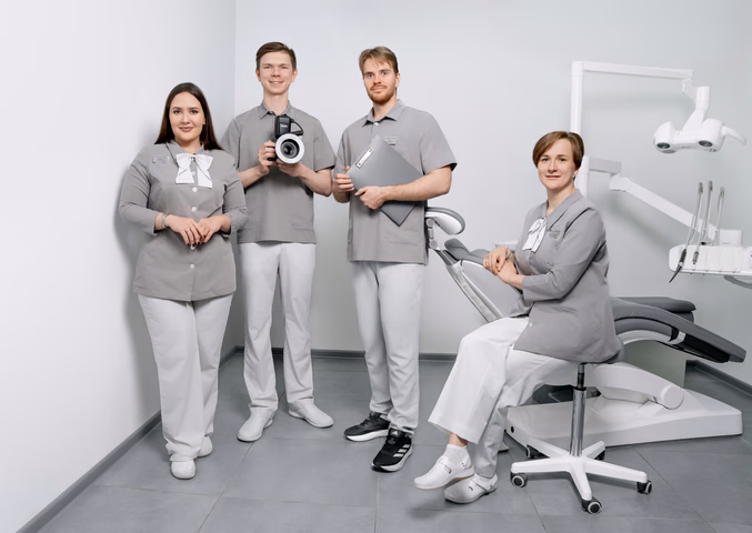 Четыре сотрудника «Стомалины» позируют у стоматологического кресла с фотоаппаратом и папкой