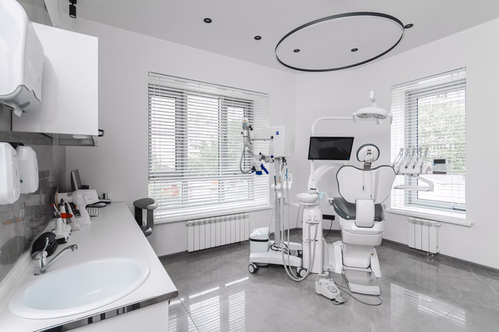Общий вид кабинета Dental Smile: раковина слева, кресло у окон и кольцевой светильник