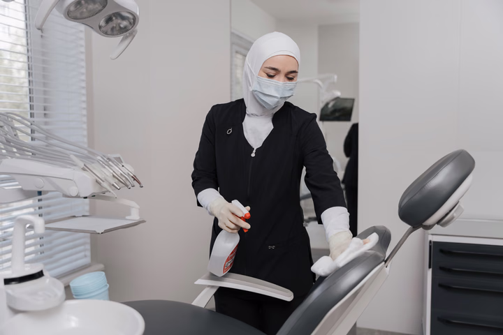 Сотрудница Dental Smile в маске протирает стоматологическое кресло и держит распылитель