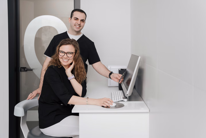 Двое сотрудников Dental Smile позируют у белого компьютерного стола в кабинете