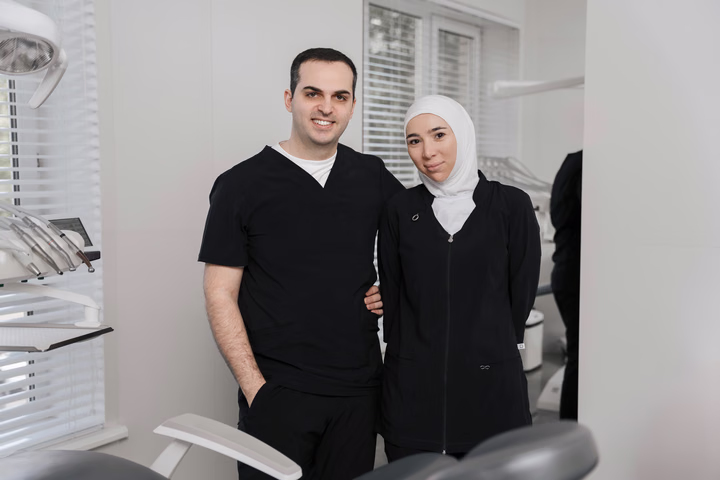 Двое сотрудников Dental Smile в чёрной форме стоят рядом у стоматологического кресла