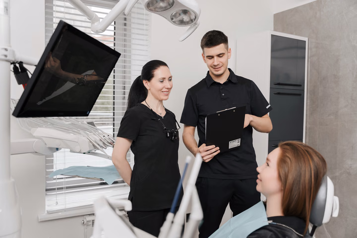 Двое сотрудников Dental Smile рассматривают планшет с бумагами рядом с пациенткой в кресле
