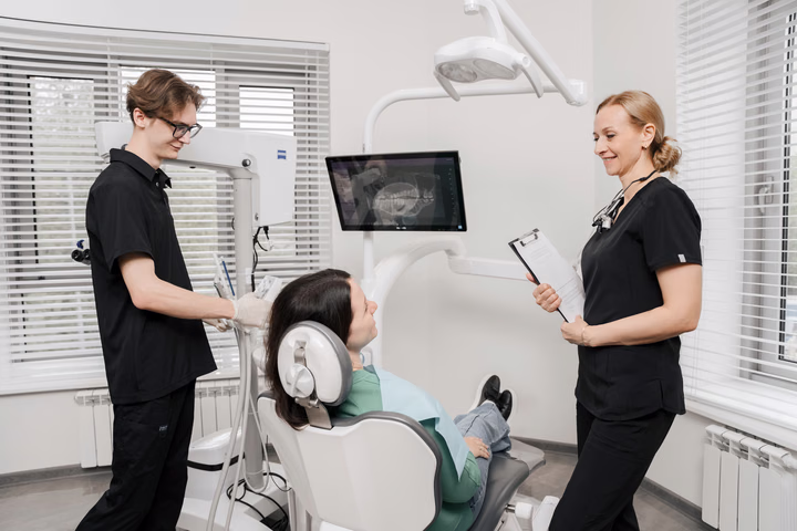 Две сотрудницы Dental Smile рядом с пациенткой: одна у кресла, другая держит планшет с бумагами