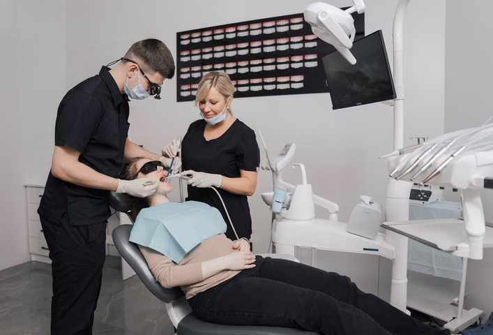 Двое сотрудников Dental Smile в масках работают с инструментами у пациентки в кресле