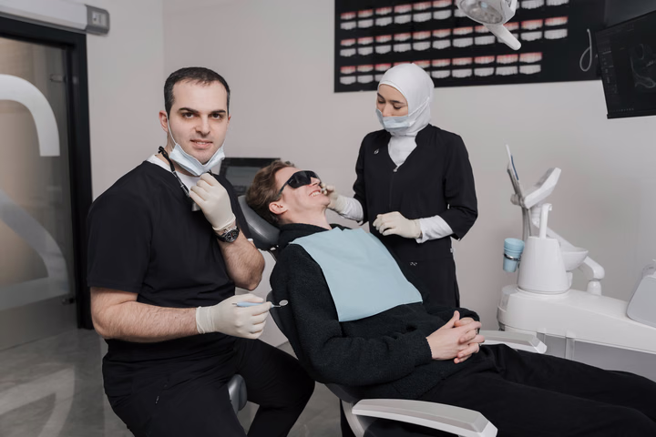 Сотрудники Dental Smile рядом с пациентом в защитных очках, сидящим в стоматологическом кресле