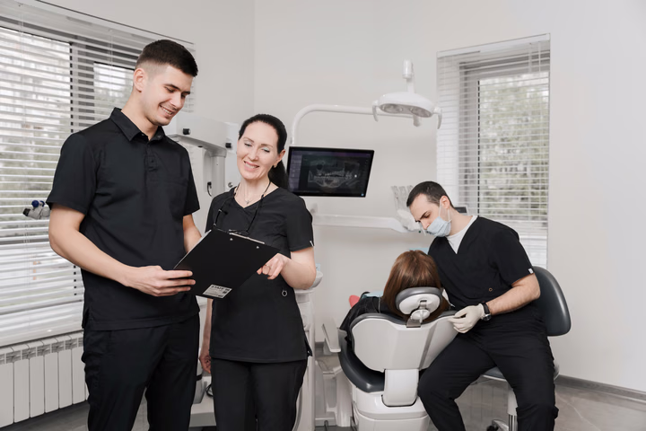 Сотрудники Dental Smile обсуждают записи, пока на заднем плане идёт приём у кресла