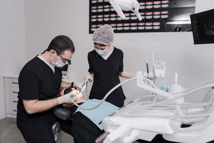 Сотрудник Dental Smile в увеличительных очках и коллега в шапочке работают у кресла пациента