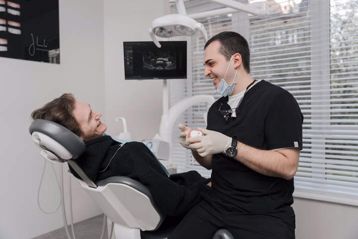 Сотрудник Dental Smile показывает модель зубов улыбающемуся пациенту в кресле