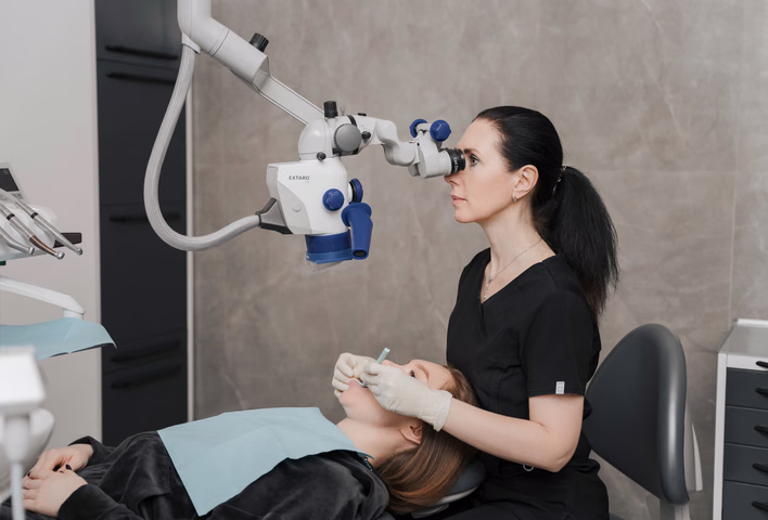 Сотрудница Dental Smile смотрит в микроскоп во время работы с пациенткой в кресле