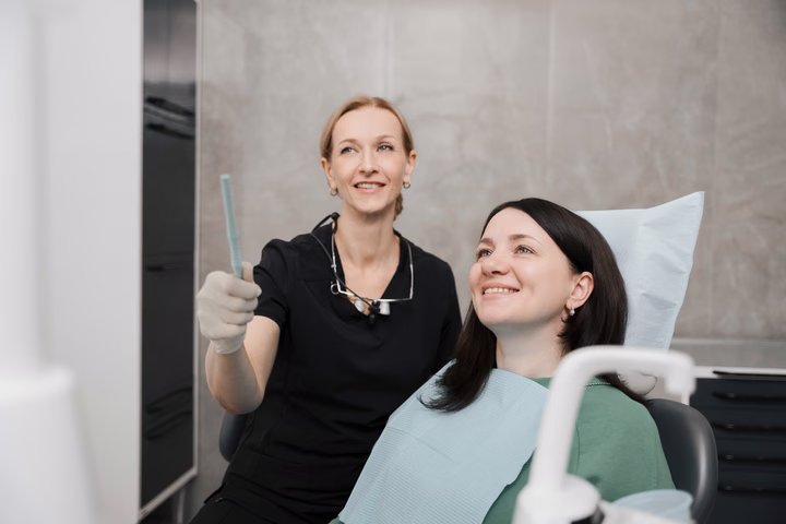 Улыбающаяся пациентка и сотрудница Dental Smile с поднятым большим пальцем в кабинете