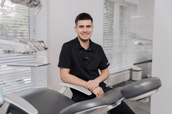 Улыбающийся сотрудник Dental Smile сидит рядом со стоматологическим креслом у окна