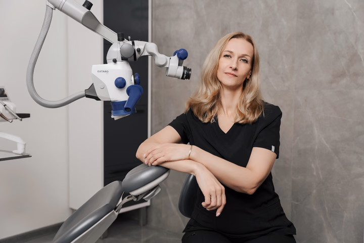 Сотрудница Dental Smile со светлыми волосами опирается руками на кресло рядом с микроскопом