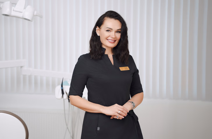 Сотрудница Simpla Dental с тёмными волнистыми волосами держит руки перед собой рядом с установкой