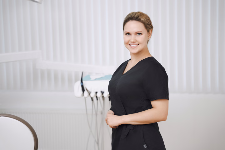Сотрудница Simpla Dental с собранными волосами улыбается, повернувшись боком к камере
