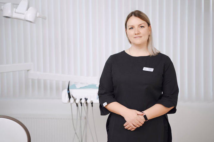 Сотрудница Simpla Dental с белым бейджем стоит лицом к камере, сложив руки перед собой