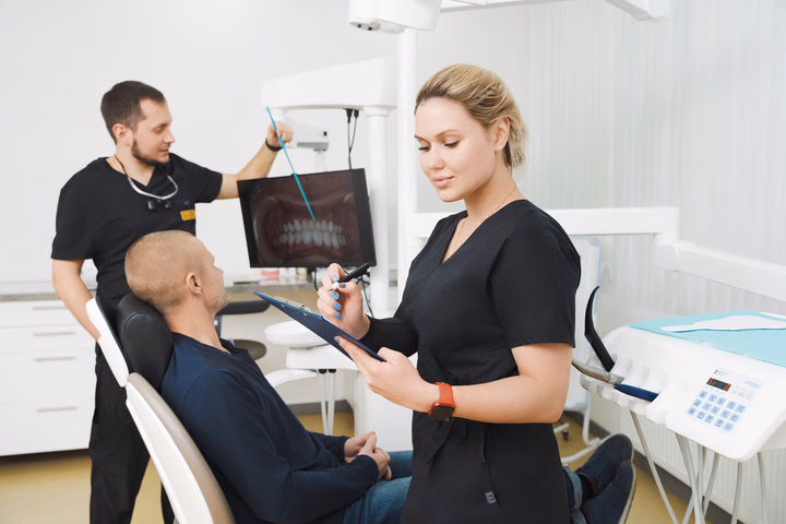 Сотрудник Simpla Dental указывает на зубы на экране, коллега делает записи рядом с пациентом