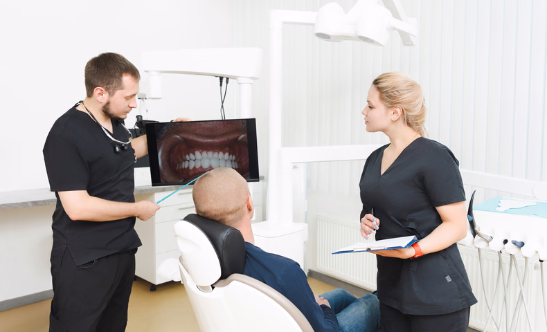 Сотрудники Simpla Dental обсуждают фотографию зубов на мониторе рядом с пациентом, вид со спины