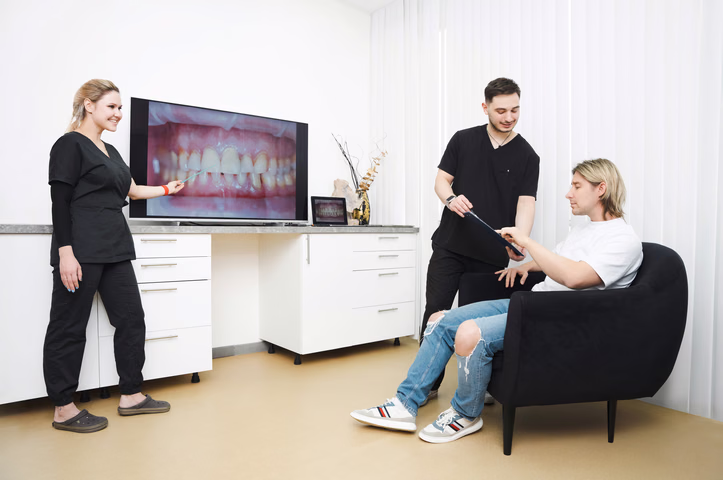 Консультация Simpla Dental у большого экрана с фотографией зубов, пациентка сидит в чёрном кресле