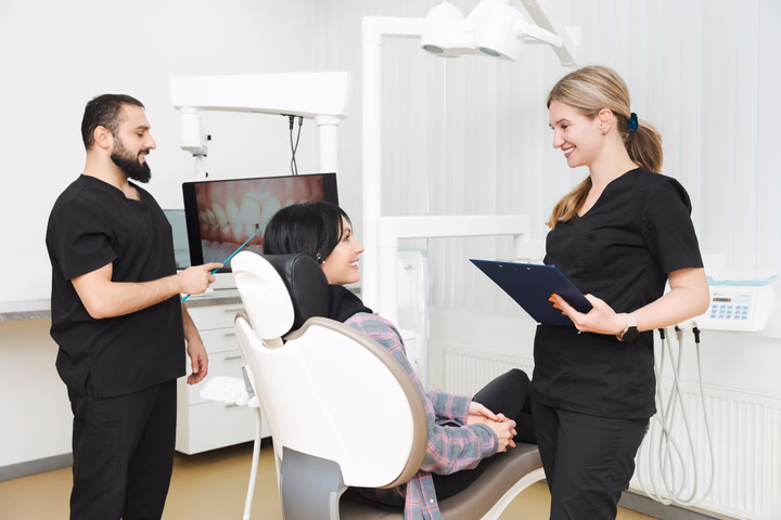 Двое сотрудников Simpla Dental беседуют с пациенткой у монитора с фотографией зубов