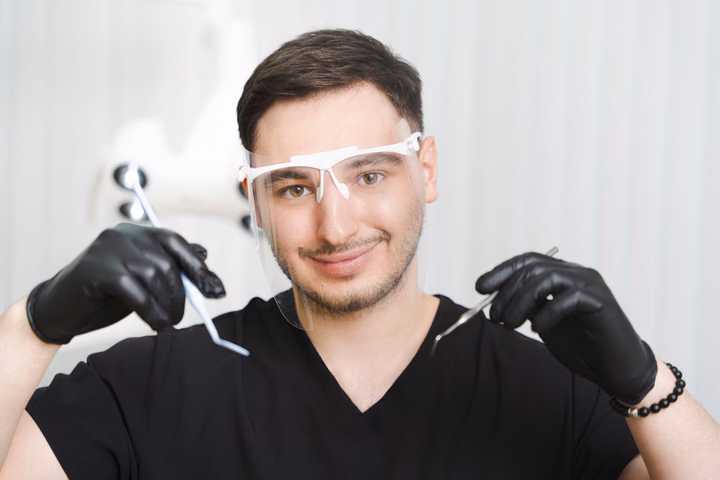 Сотрудник Simpla Dental в защитных очках и чёрных перчатках держит стоматологические инструменты
