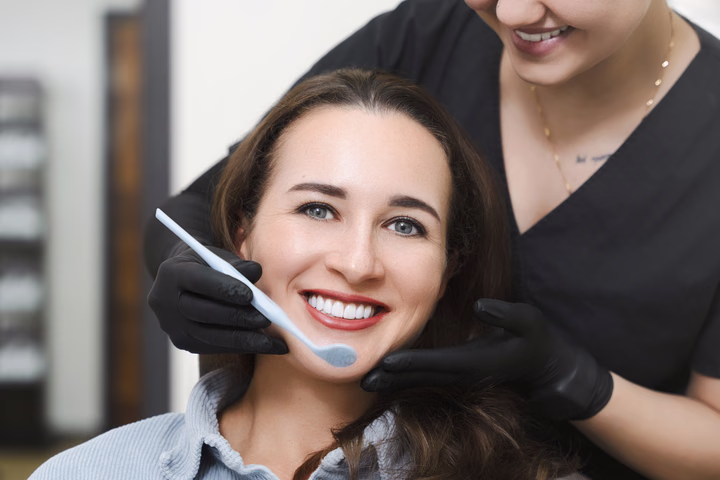 Улыбающаяся пациентка Simpla Dental и стоматологическое зеркало у её лица, крупный план