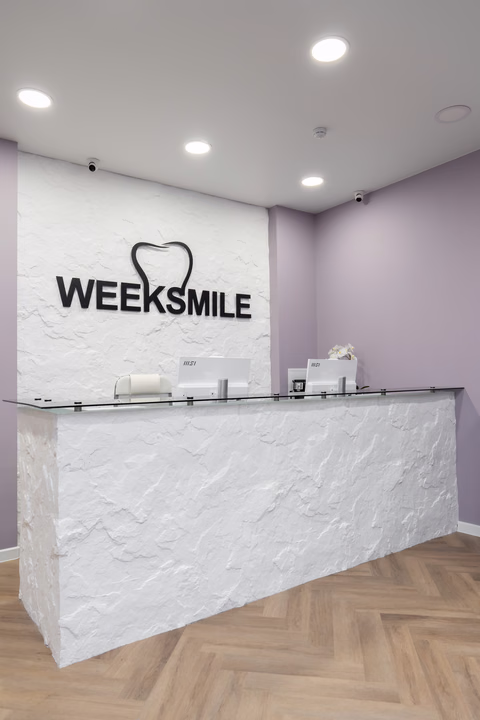 Белая стойка ресепшен Weeksmile на фоне фактурной стены с логотипом