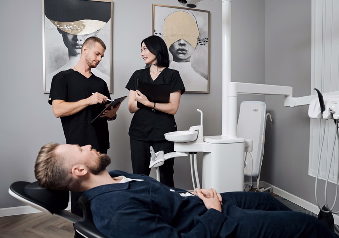 Сотрудники Weeksmile обсуждают записи на планшете возле пациента в кресле