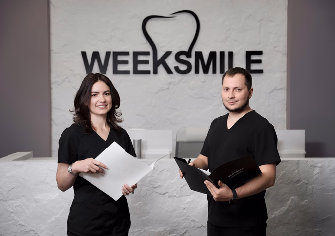 Двое сотрудников Weeksmile с документами и папкой позируют у стойки ресепшен