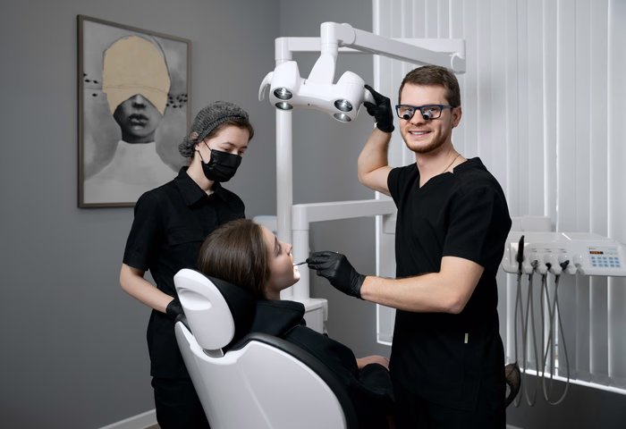 Стоматолог в очках с лупами и ассистент рядом с пациенткой под лампой Weeksmile