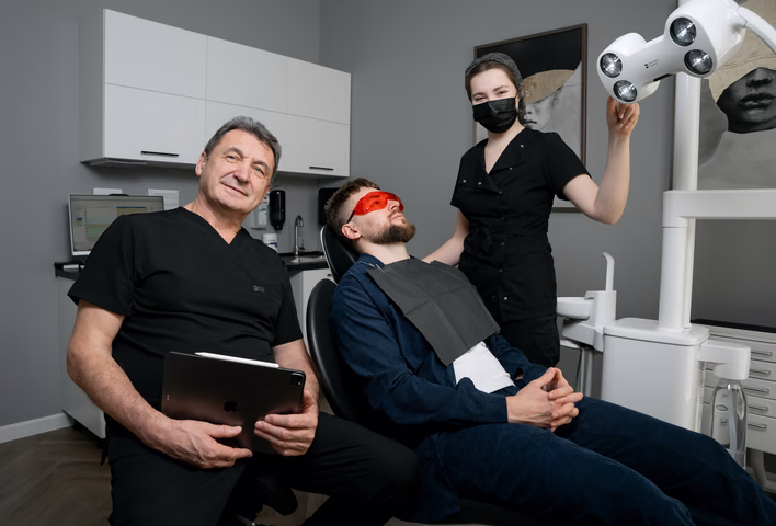Пациент в красных защитных очках рядом со стоматологом и ассистентом Weeksmile