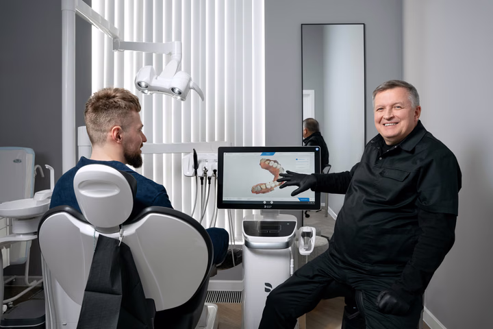 Улыбающийся стоматолог Weeksmile показывает пациенту цифровую модель зубов на экране